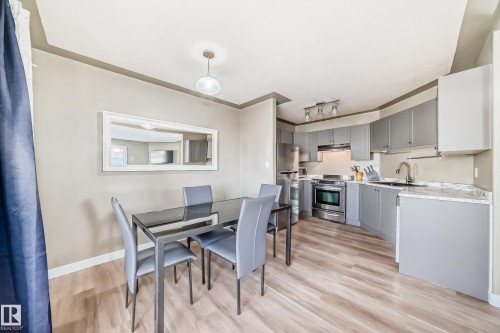 Open-concept kitchen and dining area featuring light wood-finish flooring, a contemporary dining table, a white framed mirror, modern track lighting, and grey cabinetry with stainless steel appliances - 101 10827 85 Avenue Nw, Edmonton, AB - Indoor