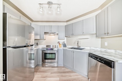 Kitchen featuring light gray cabinetry, stainless steel appliances, marble-look countertops, a black undermount sink, and wood-finish flooring - 101 10827 85 Avenue Nw, Edmonton, AB - Indoor Photo Showing Kitchen With Upgraded Kitchen