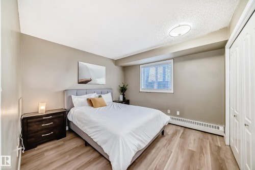 Bedroom featuring light wood-finish flooring, neutral wall tones, a window with horizontal blinds, and a built-in bi-fold door closet - 101 10827 85 Avenue Nw, Edmonton, AB - Indoor Photo Showing Bedroom