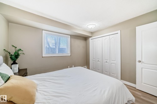 Bedroom featuring wood-finish flooring, a window with blinds, a bi-fold closet, a white interior door, and a ceiling-mounted light fixture - 101 10827 85 Avenue Nw, Edmonton, AB - Indoor Photo Showing Bedroom