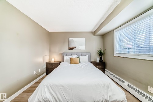 Bedroom featuring a large window with blinds, wood-finish flooring, and neutral wall tones - 101 10827 85 Avenue Nw, Edmonton, AB - Indoor Photo Showing Bedroom