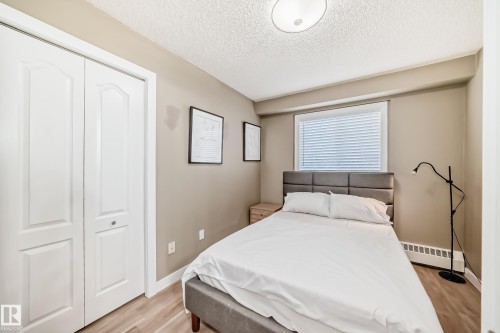 Bedroom featuring light wood-finish flooring, neutral wall tones, a window with blinds, and white bi-fold closet doors - 101 10827 85 Avenue Nw, Edmonton, AB - Indoor Photo Showing Bedroom