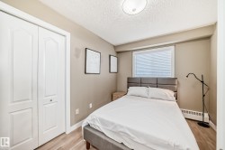 Bedroom featuring light wood-finish flooring, neutral wall tones, a window with blinds, and white bi-fold closet doors - 