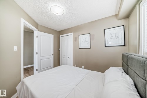 Bedroom featuring soft neutral wall paint, a white paneled door, bi-fold closet doors, and wood-finish flooring visible through the doorway - 101 10827 85 Avenue Nw, Edmonton, AB - Indoor Photo Showing Bedroom