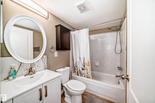 Bathroom featuring a single vanity with integrated sink, white cabinetry, and an oval framed mirror - 101 10827 85 Avenue Nw, Edmonton, AB - Indoor Photo Showing Bathroom