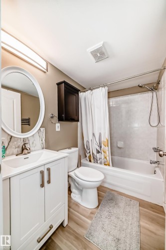 Bathroom featuring a white vanity with integrated sink, a full-size tub with shower, and wood-finish flooring - 101 10827 85 Avenue Nw, Edmonton, AB - Indoor Photo Showing Bathroom