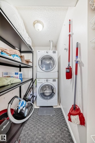 Dedicated utility space featuring a stacked washer and dryer unit, overhead lighting, durable flooring, and built-in shelving - 101 10827 85 Avenue Nw, Edmonton, AB - Indoor Photo Showing Laundry Room