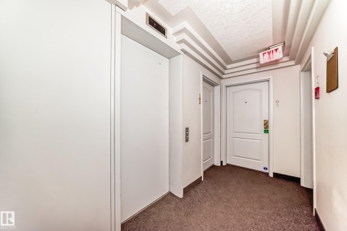Common area hallway featuring an elevator, two entry doors with paneled designs, and a textured carpeted floor - 101 10827 85 Avenue Nw, Edmonton, AB - Indoor Photo Showing Other Room