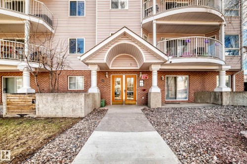 Building exterior featuring brick and siding finishes, a covered entrance with double doors, curved balconies with white railings, and a concrete pathway - 101 10827 85 Avenue Nw, Edmonton, AB - Outdoor