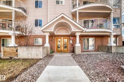 Building exterior featuring brick and siding finishes, a covered entrance with double doors, curved balconies with white railings, and a concrete pathway - 