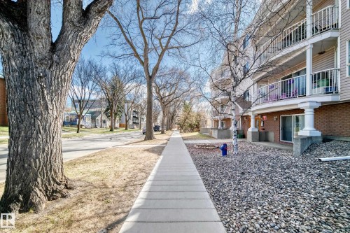 Multi-story building featuring tan horizontal siding, white balcony railings, and ground-level sliding patio doors - 101 10827 85 Avenue Nw, Edmonton, AB - Outdoor