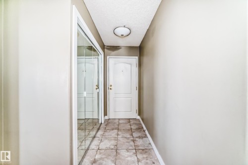 Foyer featuring neutral wall tones, square tile flooring, a white paneled door with brass hardware, and a mirrored closet door - 101 10827 85 Avenue Nw, Edmonton, AB - Indoor Photo Showing Other Room
