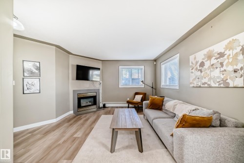 Living area featuring wood-finish flooring and a corner fireplace - 101 10827 85 Avenue Nw, Edmonton, AB - Indoor Photo Showing Living Room With Fireplace