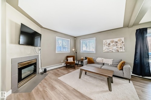 Living area featuring wood-finish flooring, a corner fireplace with tile surround, and two windows with blinds - 101 10827 85 Avenue Nw, Edmonton, AB - Indoor Photo Showing Living Room With Fireplace