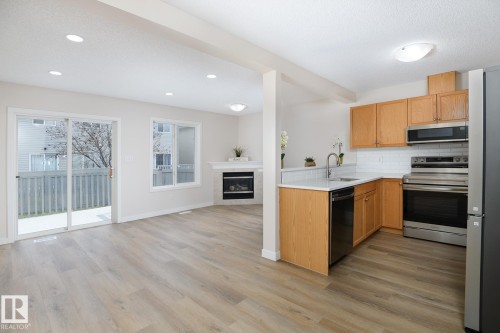 Open-concept kitchen and living area featuring wood-finish flooring, recessed lighting, and a white subway tile backsplash - 55 14603 Miller Boulevard, Edmonton, AB - Indoor Photo Showing Kitchen With Fireplace