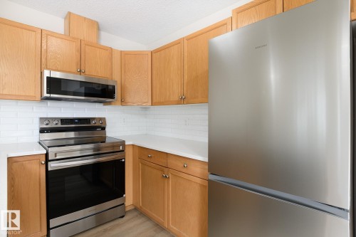 Kitchen featuring light wood cabinetry, white countertops, subway tile backsplash, and stainless steel appliances including a refrigerator, range, and microwave - 55 14603 Miller Boulevard, Edmonton, AB - Indoor Photo Showing Kitchen