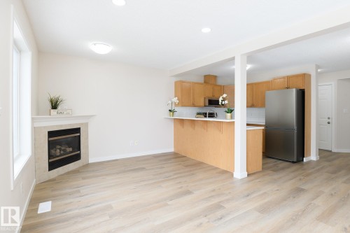 Bright open-concept living space featuring light wood-finish flooring - 55 14603 Miller Boulevard, Edmonton, AB - Indoor Photo Showing Other Room With Fireplace
