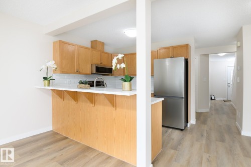 Kitchen featuring wood-finish cabinetry, white subway tile backsplash, stainless steel microwave, and stainless steel refrigerator - 55 14603 Miller Boulevard, Edmonton, AB - Indoor Photo Showing Kitchen