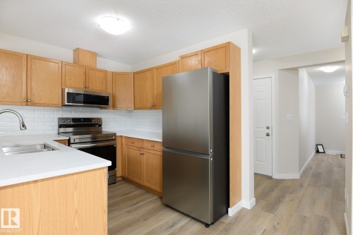 Kitchen featuring wood-finish cabinetry, stainless steel appliances, white subway tile backsplash, and light-toned countertops - 55 14603 Miller Boulevard, Edmonton, AB - Indoor Photo Showing Kitchen With Double Sink