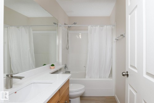 Bathroom featuring a white bathtub and shower combination, a wood-finish vanity with an integrated white sink, a brushed nickel faucet, and a large wall-mounted mirror - 55 14603 Miller Boulevard, Edmonton, AB - Indoor Photo Showing Bathroom