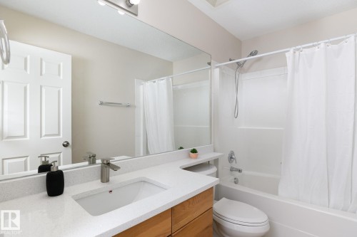 Full-size bathroom featuring a light wood-finish vanity with a white countertop and integrated sink, brushed nickel faucet, and a large wall-mounted mirror - 55 14603 Miller Boulevard, Edmonton, AB - Indoor Photo Showing Bathroom