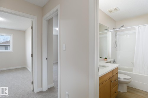 Bathroom featuring a wood-finish vanity with a light-toned countertop, integrated sink, and mirror - 55 14603 Miller Boulevard, Edmonton, AB - Indoor Photo Showing Bathroom