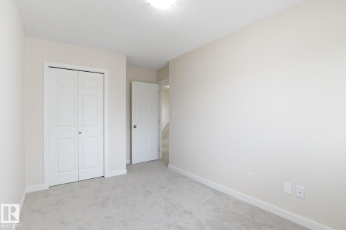 Neutral-toned room featuring light gray carpeting, white baseboards, and a bi-fold closet with panel detailing - 55 14603 Miller Boulevard, Edmonton, AB - Indoor