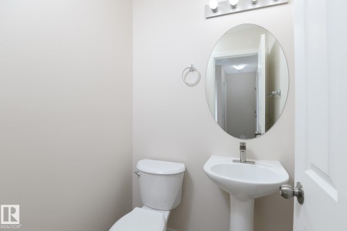 Powder room featuring a pedestal sink with a chrome faucet, an oval mirror, and a three-light vanity fixture - 55 14603 Miller Boulevard, Edmonton, AB - Indoor Photo Showing Bathroom