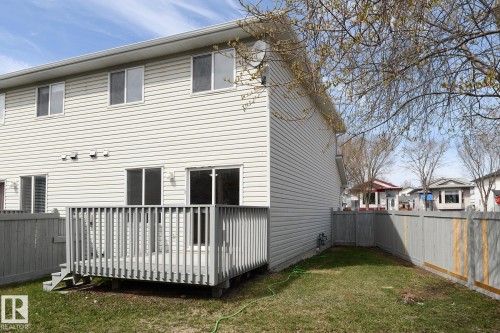 Rear exterior featuring a spacious wooden deck with railings, vinyl siding, and a fenced backyard with a grassy area - 55 14603 Miller Boulevard, Edmonton, AB - Outdoor