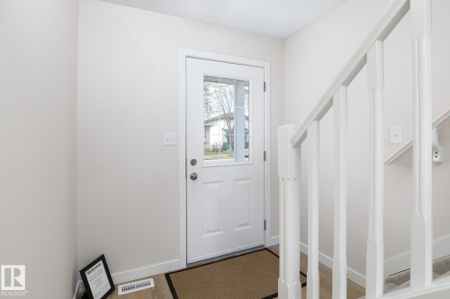 Entryway featuring a white paneled door with window inserts, light-colored walls, wood-finish flooring, and a white staircase with balusters - 55 14603 Miller Boulevard, Edmonton, AB - Indoor Photo Showing Other Room