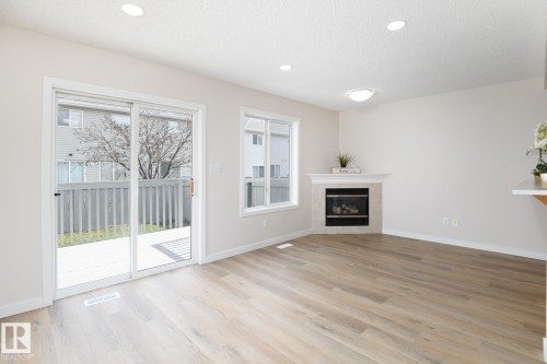 Spacious room featuring wood-finish flooring, a corner fireplace with a white mantel, and recessed ceiling lighting - 55 14603 Miller Boulevard, Edmonton, AB - Indoor Photo Showing Living Room With Fireplace
