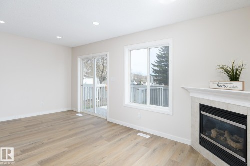 Living area featuring wood-finish flooring, a corner fireplace with a tile surround and mantel, a sliding glass door leading to an outdoor deck, a large window, and recessed ceiling lighting - 55 14603 Miller Boulevard, Edmonton, AB - Indoor With Fireplace
