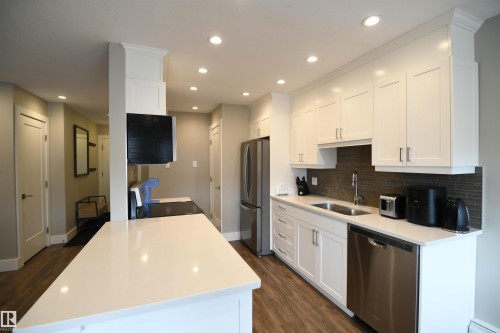 Solid surface counters with an undermount sink, contemporary white cabinetry, tile backsplash, ample pot lights, stainless appliance package, and an inviting, open layout - 206 8125 110 Street, Edmonton, AB - Indoor Photo Showing Kitchen With Double Sink With Upgraded Kitchen