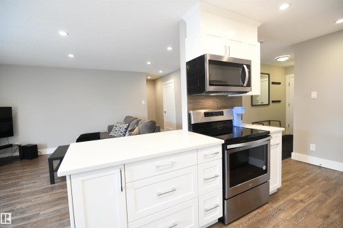 Solid surface counters with an undermount sink, contemporary white cabinetry, tile backsplash, ample pot lights, stainless appliance package, and an inviting, open layout - 206 8125 110 Street, Edmonton, AB - Indoor Photo Showing Kitchen