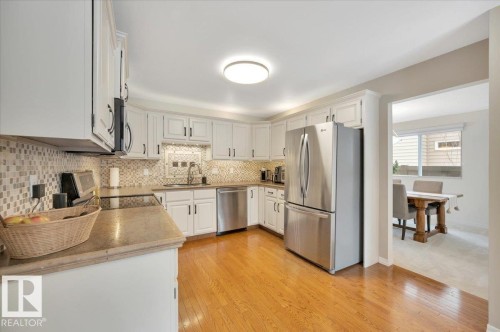 The kitchen features white cabinetry, stainless steel appliances, hardwood floors, and a tiled backsplash - 705 Riddell Street, Edmonton, AB - Indoor Photo Showing Kitchen With Upgraded Kitchen