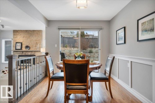 features hardwood floors, patio door opening onto the deck providing backyard views, and wainscoting detail on the wall - 705 Riddell Street, Edmonton, AB - Indoor Photo Showing Dining Room