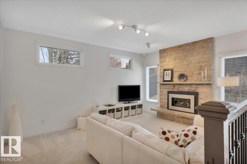 Living area featuring a stone accent wall with a fireplace, track lighting, and rectangular windows - 705 Riddell Street, Edmonton, AB - Indoor Photo Showing Living Room With Fireplace