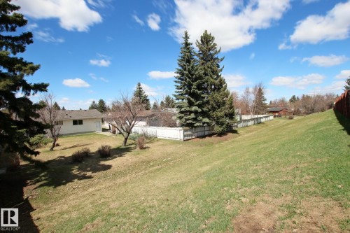 Expansive sloped lawn area with mature evergreen trees and white perimeter fencing - 3539 104 Street, Edmonton, AB - Outdoor