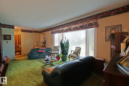 Spacious living area featuring a large picture window with white blinds, wood-finish flooring, and a built-in room divider - 3539 104 Street, Edmonton, AB - Indoor Photo Showing Living Room