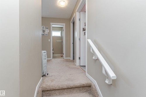 Carpeted hallway with light neutral wall paint and white trim, featuring a flush mount ceiling light, a built-in white handrail, and two interior doorways - 4452 Annett Common, Edmonton, AB 