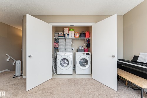 In-unit laundry closet featuring a stacked washer and dryer, wire shelving, and overhead storage - 4452 Annett Common, Edmonton, AB 
