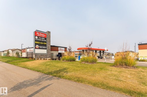 Retail center featuring a stone-clad pylon sign, a drive-thru building, a gas station canopy with red accents, and manicured landscaping - 4452 Annett Common, Edmonton, AB 