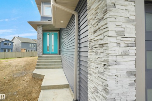 Modern exterior showcasing a vibrant turquoise entry door with vertical glass inserts, gray horizontal siding, and a stone-clad architectural pillar - 22139 81 Avenue, Edmonton, AB - Outdoor