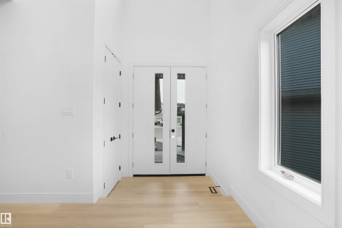 Bright entryway featuring double glass-paneled doors, a large casement window with interior blinds, light wood-finish flooring, and white baseboards - 22139 81 Avenue, Edmonton, AB - Indoor Photo Showing Other Room