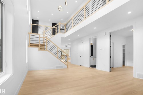 Two-story entry featuring light wood-finish flooring, a contemporary staircase with horizontal metal balusters, recessed lighting, and a white interior palette - 22139 81 Avenue, Edmonton, AB - Indoor Photo Showing Other Room