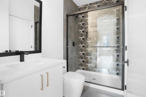 Contemporary bathroom featuring a frameless glass shower enclosure with matte black hardware, a custom hex-patterned tile shower surround, a white vanity with a single basin sink and matte black faucet, and a large black-framed mirror - 22139 81 Avenue, Edmonton, AB - Indoor Photo Showing Bathroom