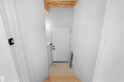 Unfinished lower level space with drywall installation, exposed ceiling joists, wood stairs, and a paneled entry door - 22139 81 Avenue, Edmonton, AB - Indoor Photo Showing Other Room