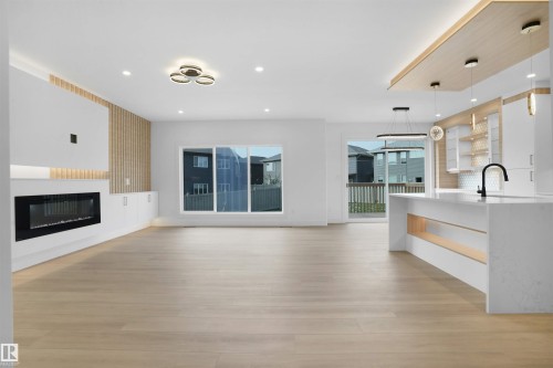 Open-concept living space featuring wood-finish flooring, a linear electric fireplace with built-in cabinetry, and a kitchen island with integrated shelving - 22139 81 Avenue, Edmonton, AB - Indoor Photo Showing Other Room With Fireplace