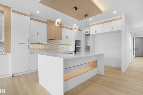 Contemporary kitchen featuring a waterfall island with integrated shelving, light wood-finish flooring, white cabinetry with gold-toned hardware, a hexagonal tile backsplash, and recessed lighting - 22139 81 Avenue, Edmonton, AB - Indoor Photo Showing Kitchen With Upgraded Kitchen
