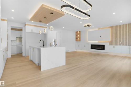 Open-concept living space featuring light wood-finish flooring, a contemporary fireplace, and a kitchen island with a waterfall countertop - 22139 81 Avenue, Edmonton, AB - Indoor With Fireplace